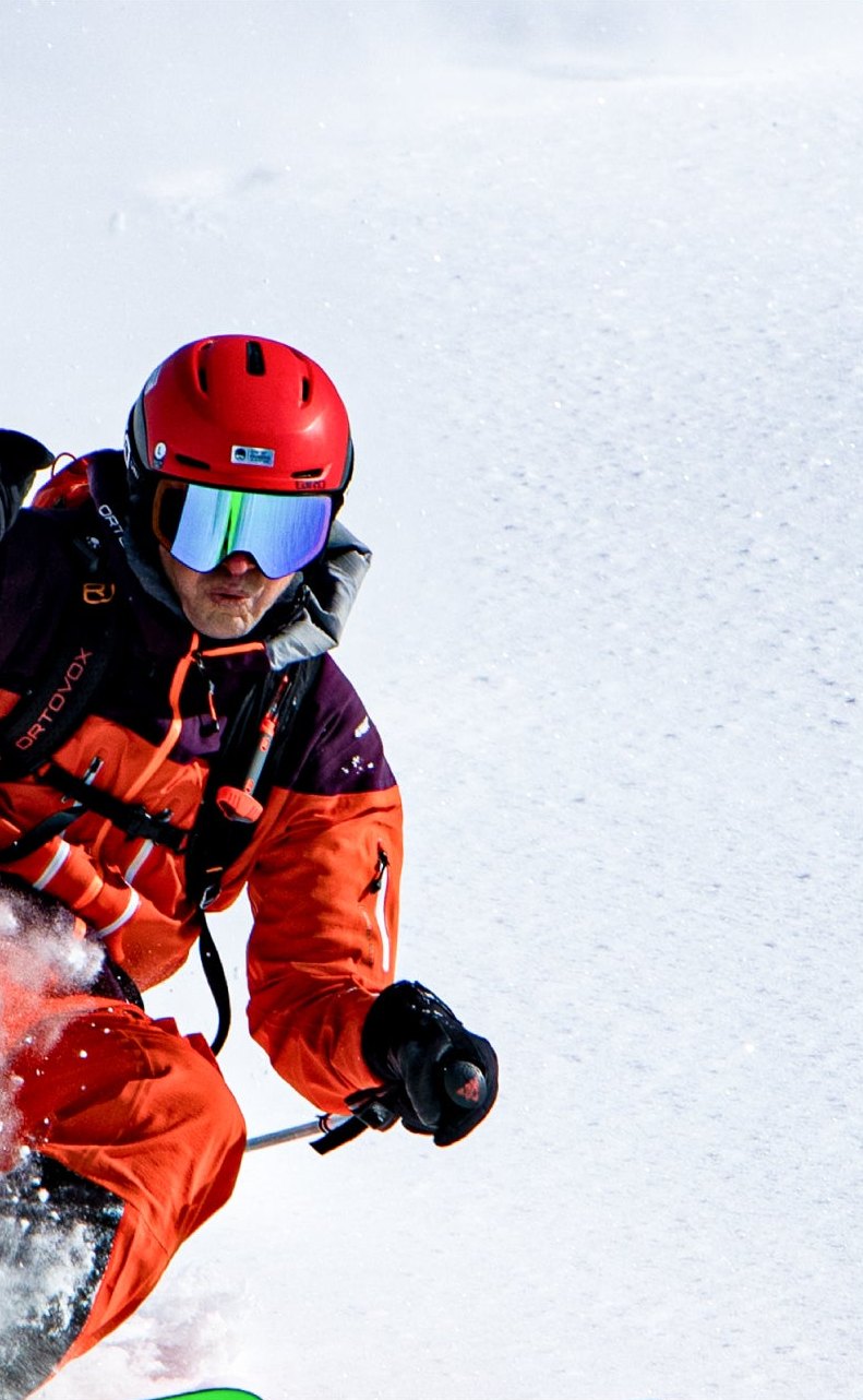 Skifahrer mit rotem Helm und verspiegelter Skibrille fährt durch hellen Tiefschnee